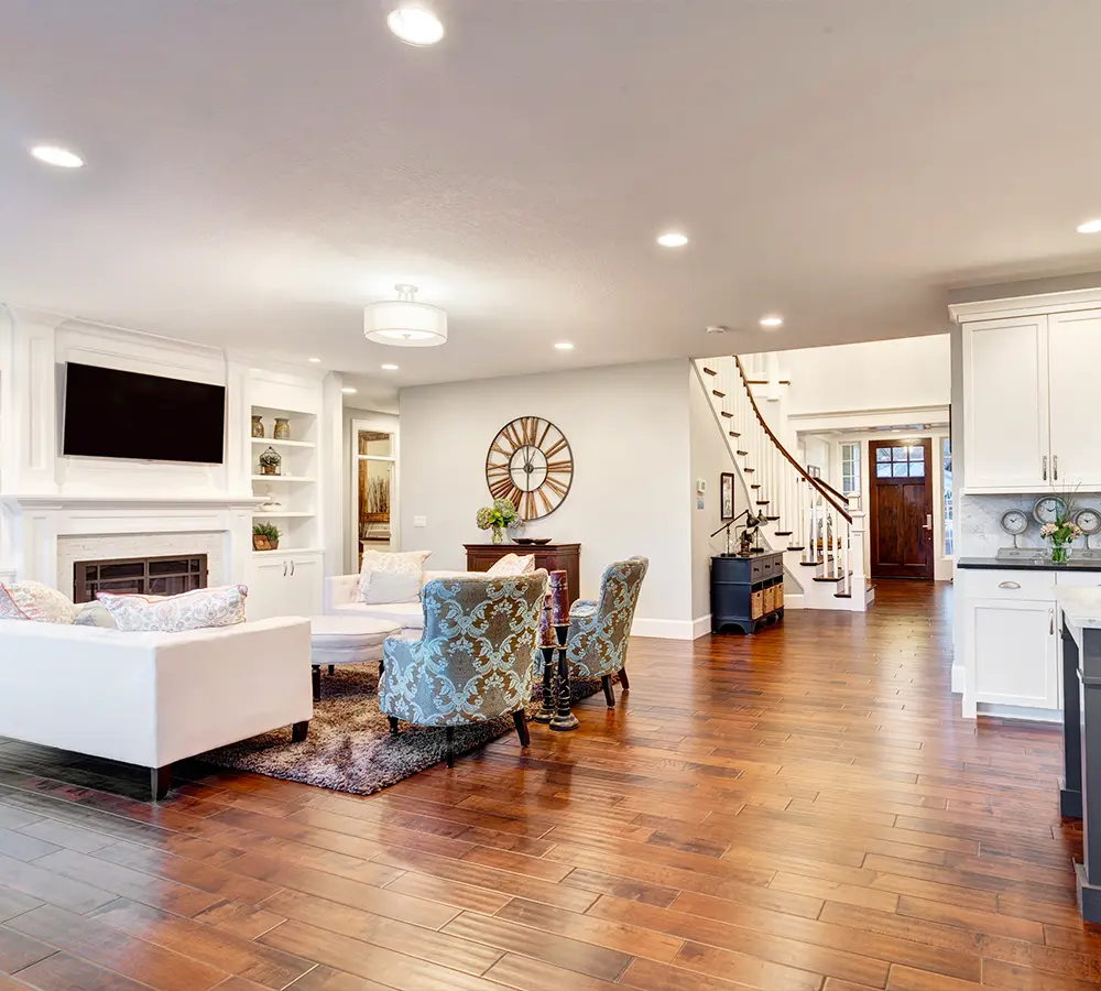 Spacious living room with hardwood floors, cozy seating, white fireplace, and a staircase leading to the second floor.