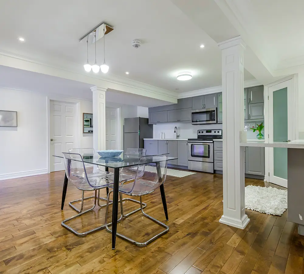 Open-concept basement dining area with glass table and hardwood floors.