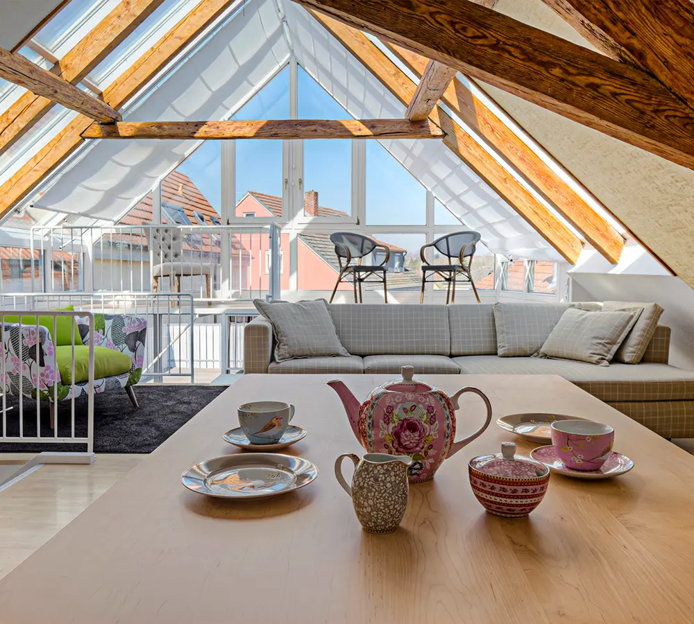 Trendy attic space converted into a bright lounge with exposed wooden beams and expansive windows.