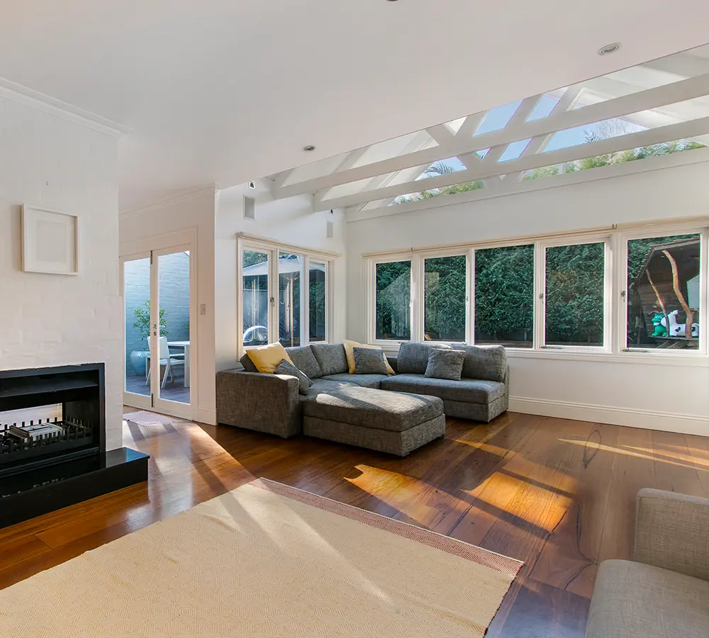 Bright living room featuring large windows, a modern fireplace, and white wooden ceiling beams.