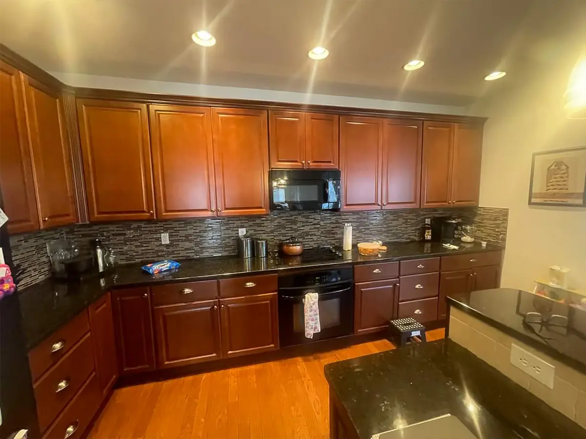 Before home renovation with outdated wooden cabinetry and black countertops.