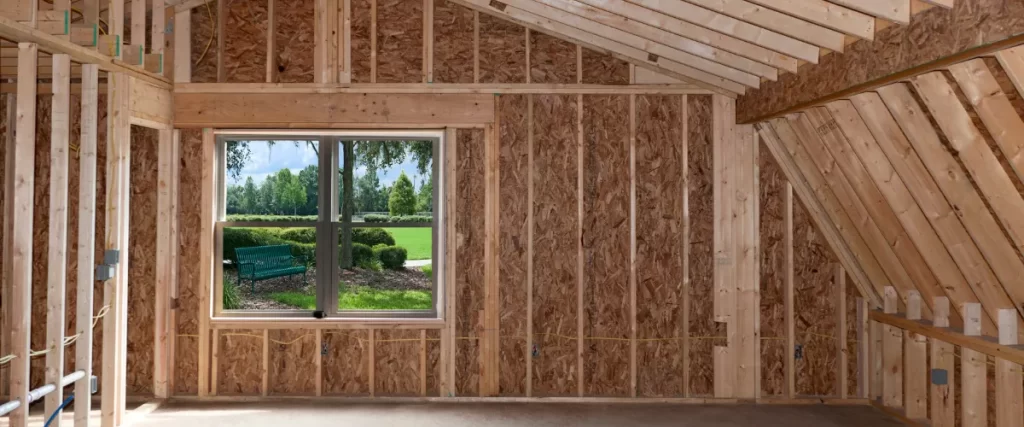 Interior view of a partially constructed room with exposed wood framing and a window showing a green outdoor landscape (selected).

