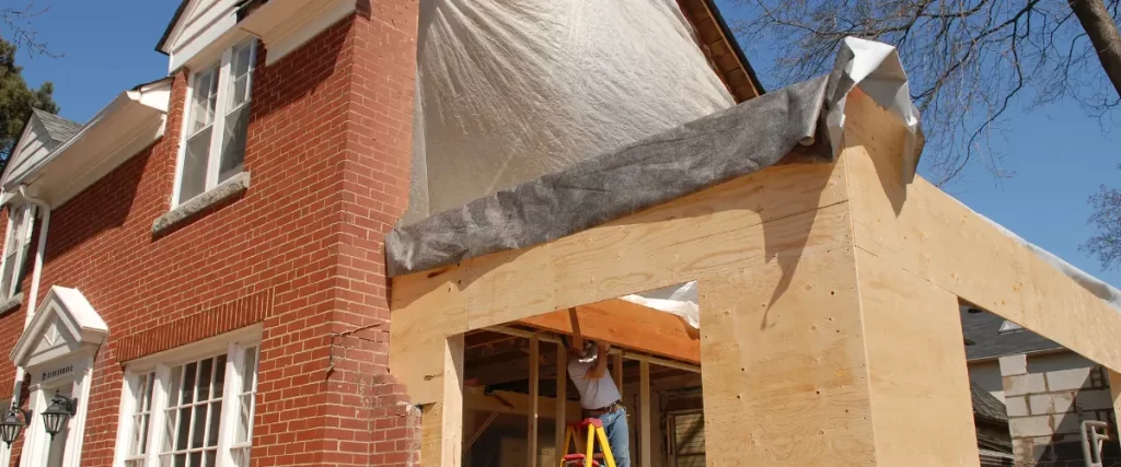 Contractor working on home addition with exposed plywood and plastic sheeting